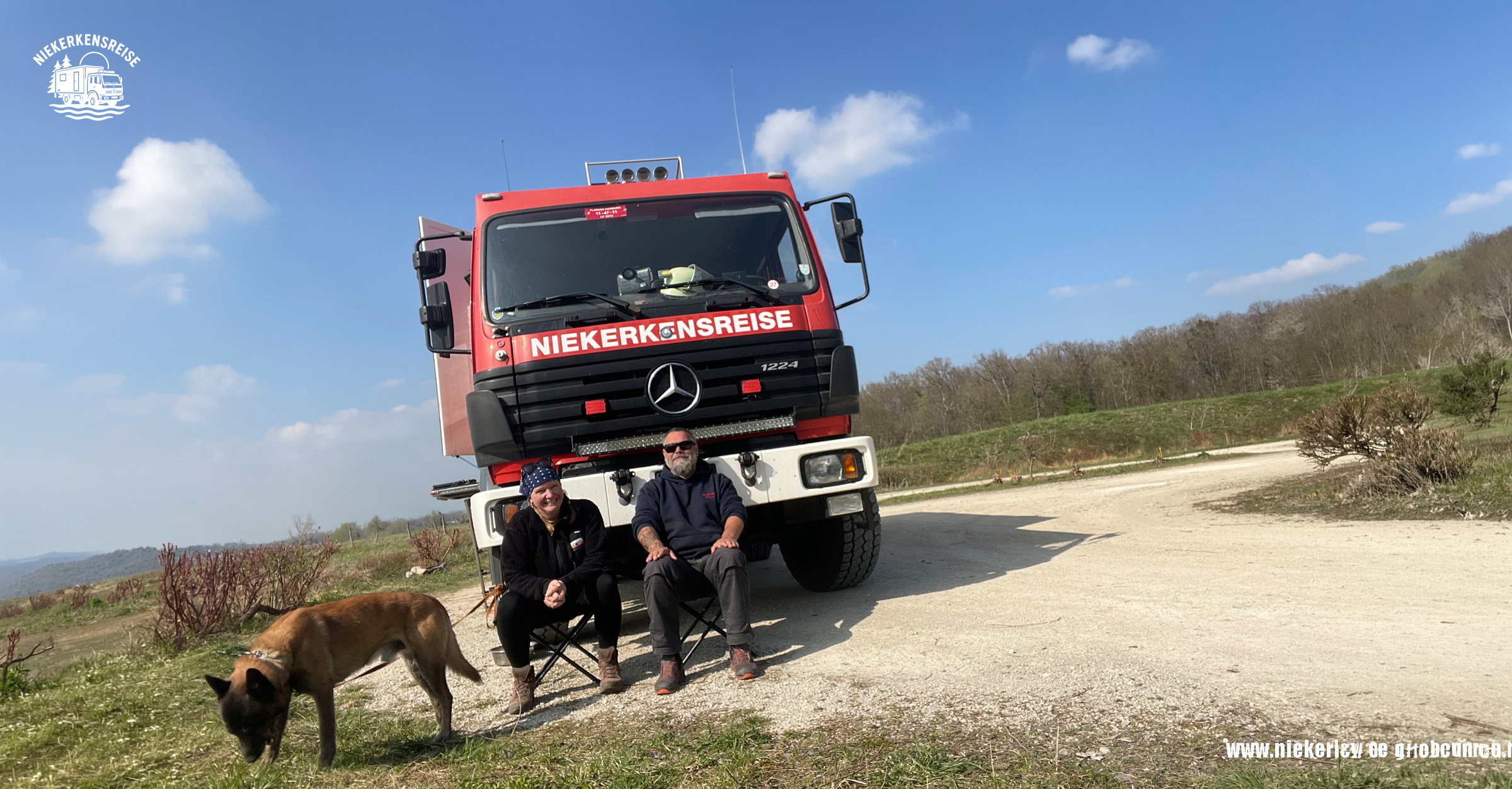 Anja, Lars und Elvis – Das Team hinter Niekerkensreise Anja und Lars Niekerken sitzen vor ihrem roten Mercedes-Benz 1224 AF Feuerwehr-LKW, während Hund Elvis im Vordergrund schnüffelt. Niekerkensreise unterwegs mit dem Expeditionsmobil.
