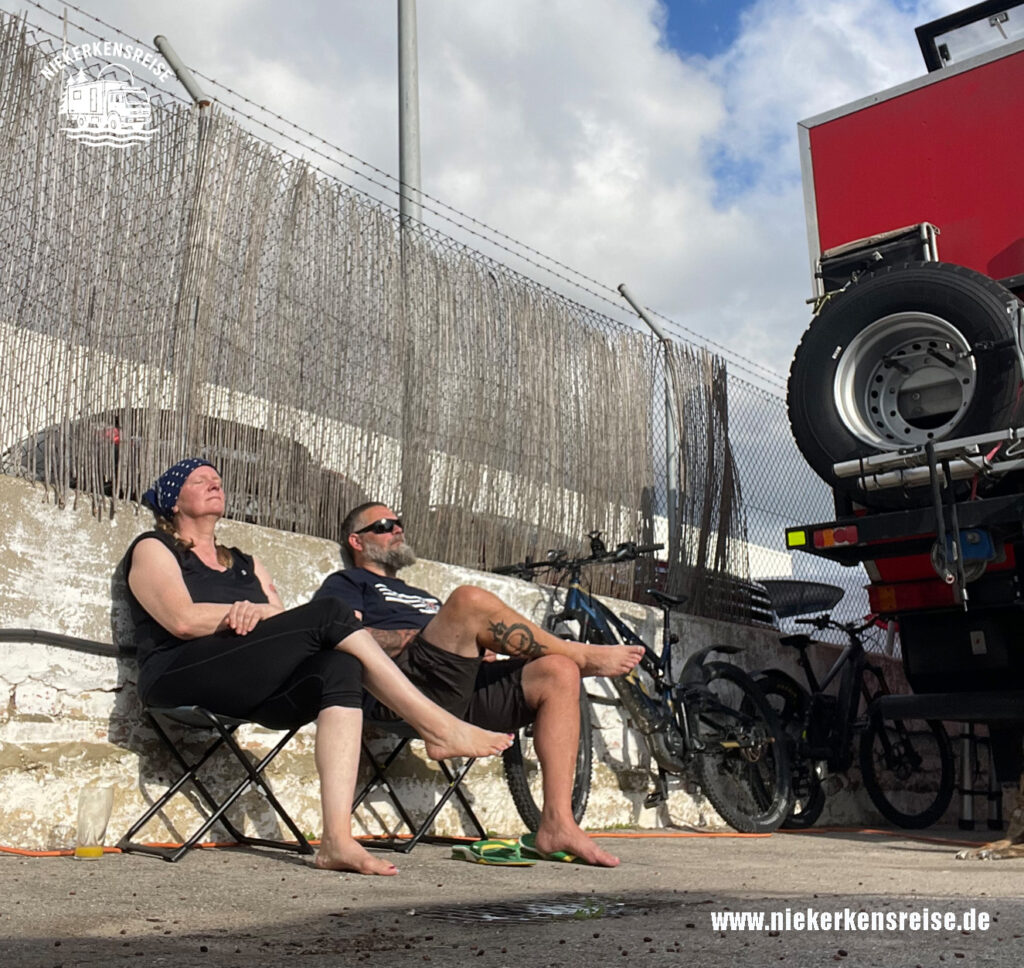 Anja und Lars machen Siesta im Schatten ihres LKW-Campers – Entspannung und Hitzeschutz beim Camping im Sommer
