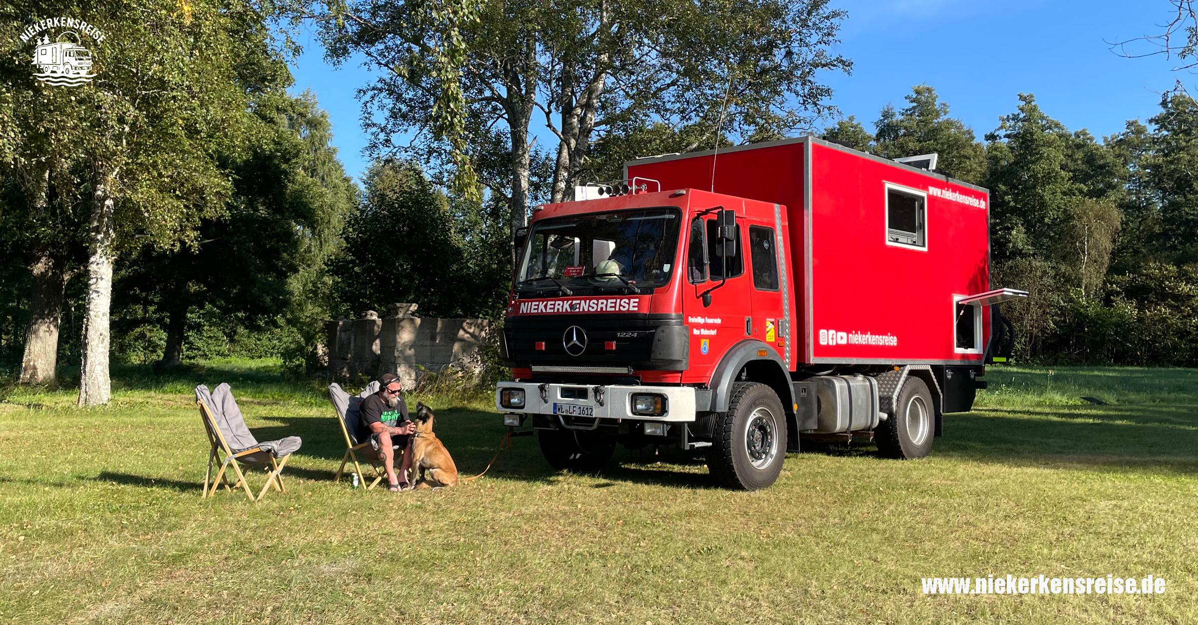 Anja und Lars von Niekerkensreise sitzen mit ihrem Hund vor ihrem roten Mercedes Benz 1224 4x4 Feuerwehr-LKW, den sie zum Expeditionsmobil ausgebaut haben. Unterwegs im Grünen genießen sie das Leben im selbst ausgebauten Wohnmobil und teilen ihre Reiseerfahrungen, Alltagstipps sowie Ausbau- und Reparaturvideos mit Camping- und Offroad-Fans.