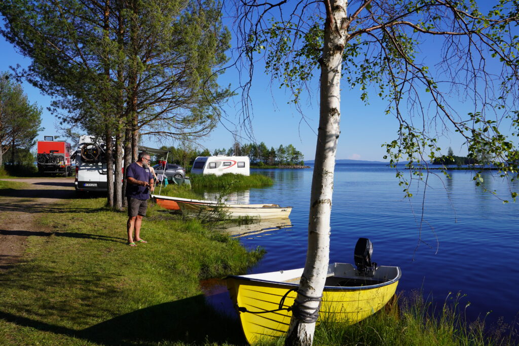 Mann - Lars - am See mit Booten und Campern am Ufer eines Campingplatzes in Schweden bei sonnigem Wetter.