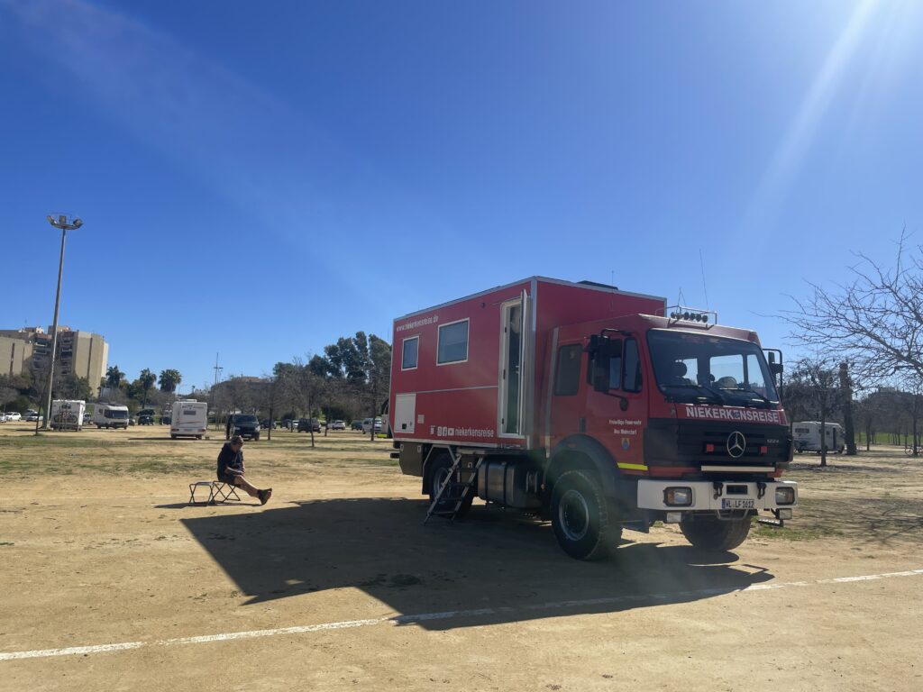 Zum Wohnmobil umgebauter Feuerwehr LKW auf einem Sandparkplatz in Sevilla