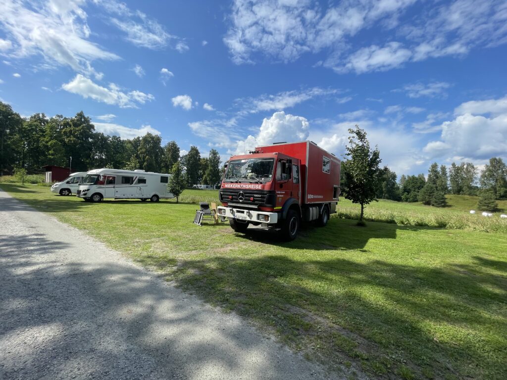 Feuerwehr-LKW Mercedes 1224 4x4 auf dem Campingplatz Skeda Strand in Schweden neben Wohnmobilen auf einer großen Wiese.