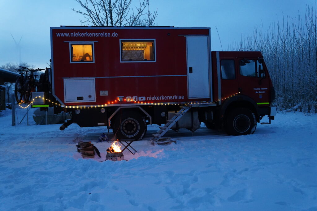 LKW Wohnmobil im Winter mit Schnee und Lagerfeuer – Leben im Wohnmobil mit festem Standort
