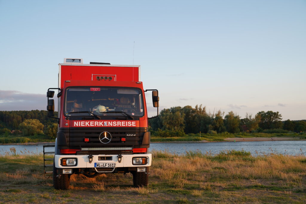 Rotes Expeditionsmobil beim Freistehen auf einer Wiese direkt am Wasser inmitten der Natur.