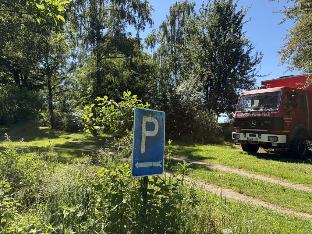 Rotes Expeditionsmobil auf einem ausgewiesenen Parkplatz inmitten einer grünen, bewaldeten Landschaft.