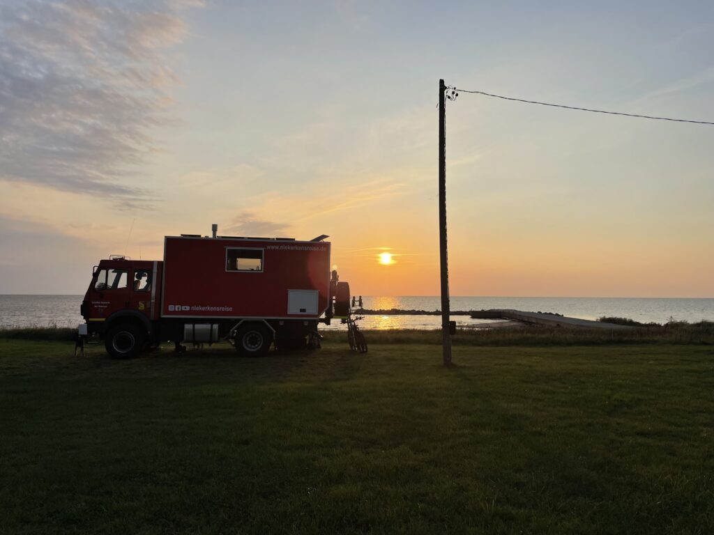 Rotes Expeditionsmobil beim Freistehen direkt am Meer während des Sonnenuntergangs.