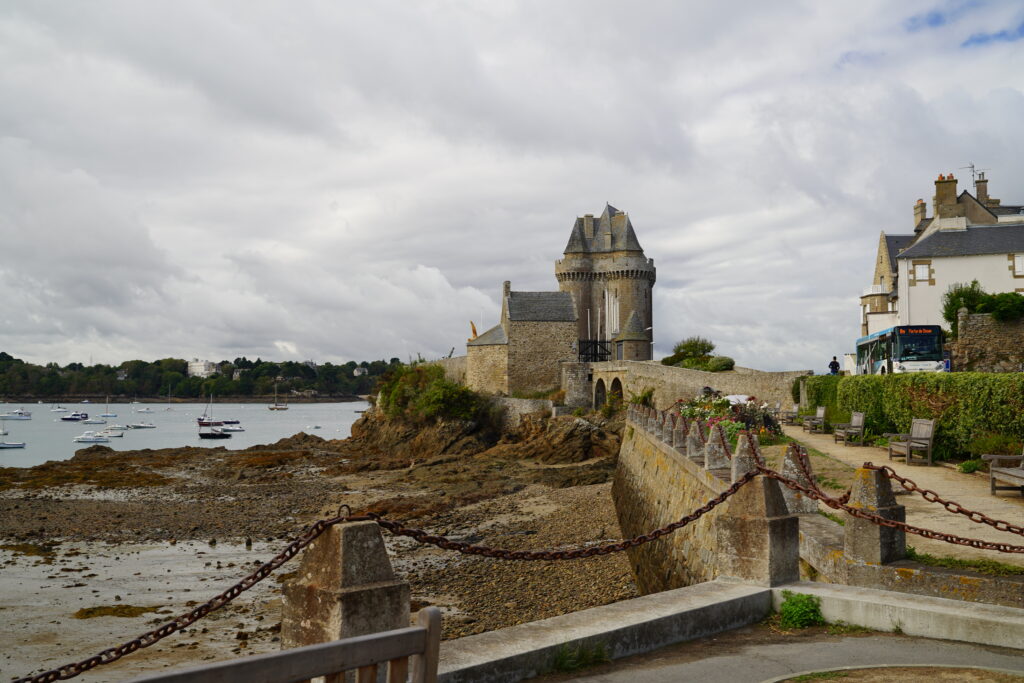 Küstenlandschaft bei Saint-Malo in der Bretagne mit historischem Steinturm, Stadtmauer, Hafen und Booten bei Ebbe.