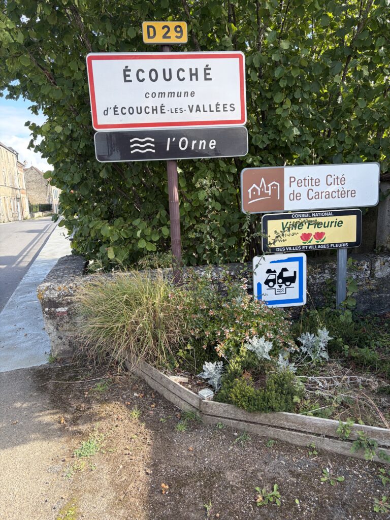 Ortsschild von Écouché-les-Vallées in der Normandie mit Wohnmobil-Symbol, Zwischenstopp auf der mautfreien Route nach Saint-Malo.