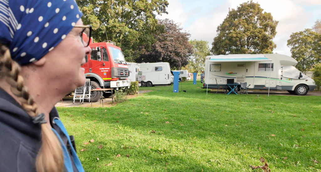 Blick auf den kostenlosen Wohnmobilstellplatz Solre-le-Château in Nordfrankreich mit mehreren Wohnmobilen, grünen Stellflächen und dem roten Expeditions-Lkw von Niekerkensreise.