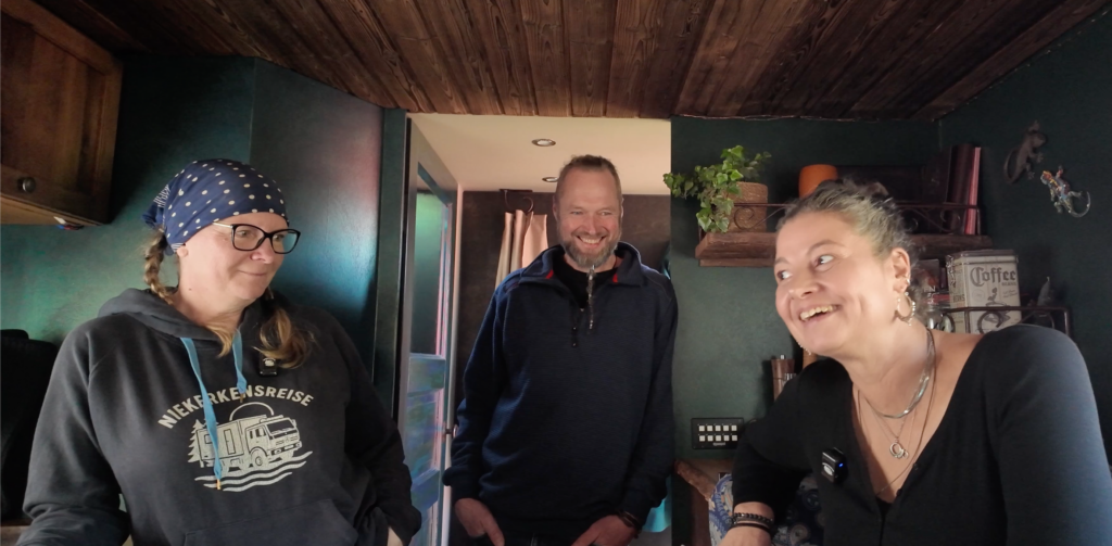 Anja von Niekerkensreise bei einer Roomtour mit Katrin und Andre im selbst ausgebauten Mercedes 1222 „Otto“. Gemütlicher Wohnmobil-Innenausbau mit Holzdecke und dunkelgrünen Wänden.
