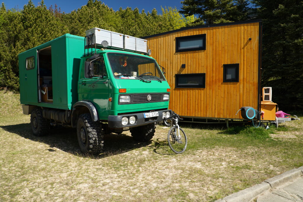Grüner VW LT Allrad-Expeditionscamper mit Wohnkoffer und großen Geländereifen beim Overlander-Treffen Quaduxenbarg 2026, neben einem Tiny House aus Holz.