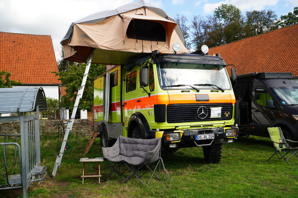 Zum Familien-Wohnmobil umgebauter Mercedes-Benz Feuerwehr-LKW TLF 1428 mit grün-orangefarbener Lackierung und großem Dachzelt beim Hof & Hubraum Treffen 2026.