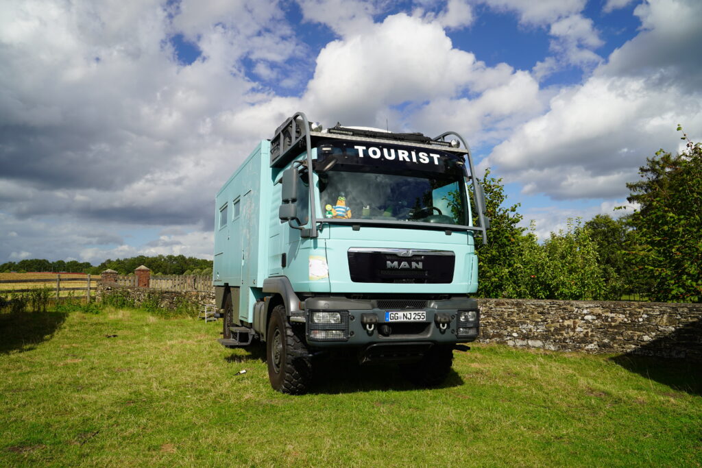 Türkisfarbener MAN 4x4 Allrad-LKW mit Expeditionsmobil-Wohnkabine, Hubdach und großen Geländereifen beim Hof & Hubraum Treffen 2026. Das Fahrzeug mit der Aufschrift „TOURIST“ steht auf einer grünen Wiese.