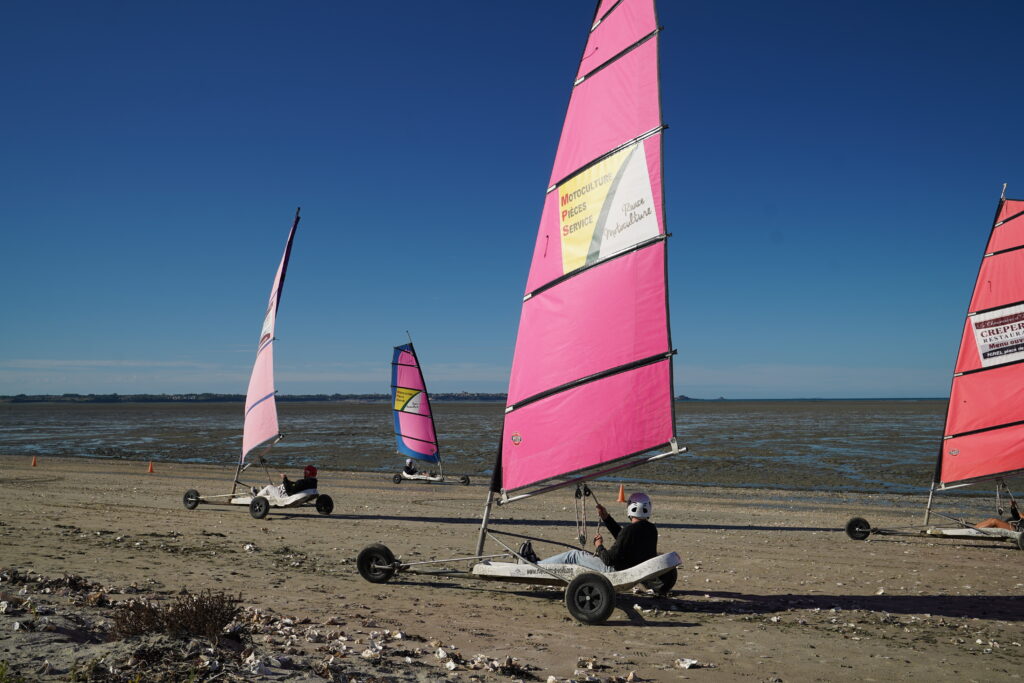 Strandsegler mit leuchtend pinkfarbenen Segeln fahren bei Ebbe über den breiten Sandstrand von Hirel in der Bretagne an der Bucht des Mont-Saint-Michel.