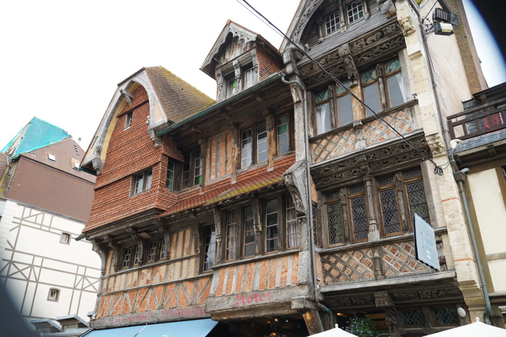 Historisches Fachwerkhaus mit kunstvoll geschnitzten Holzbalken, roten Ziegeln und dekorativen Fenstern im Ortszentrum von Étretat in der Normandie. Das traditionelle Gebäude beherbergt ein Hotel und Restaurant.
