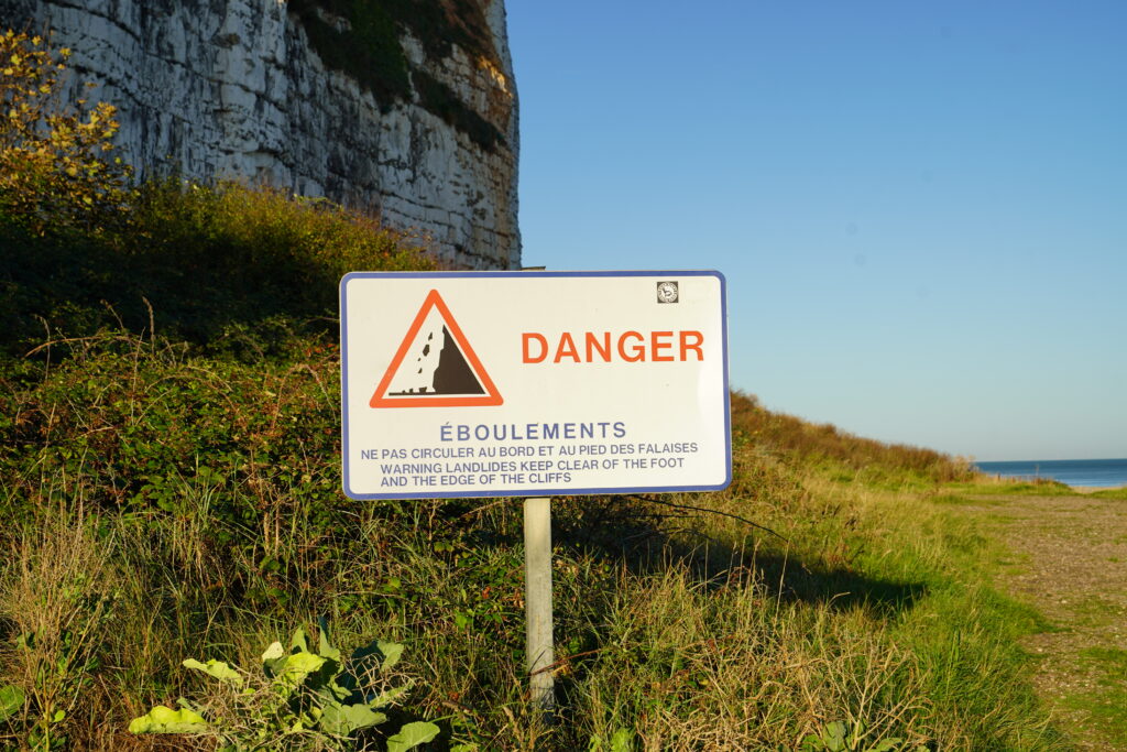 Warnschild vor Steinschlag und Felsabbrüchen an den weißen Kreidefelsen von Saint-Valery-en-Caux in der Normandie, nahe dem Wohnmobilstellplatz an der Alabasterküste.