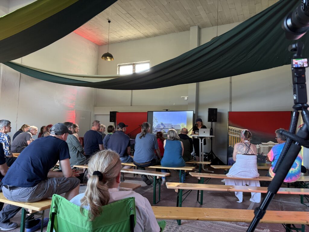 Anja Niekerken liest bei der Buchpremiere von „Kein Reisebuch“ vor Publikum auf dem Overlander-Treffen Quaduxenbarg 2026. Besucher sitzen auf Bierbänken und verfolgen die Lesung.