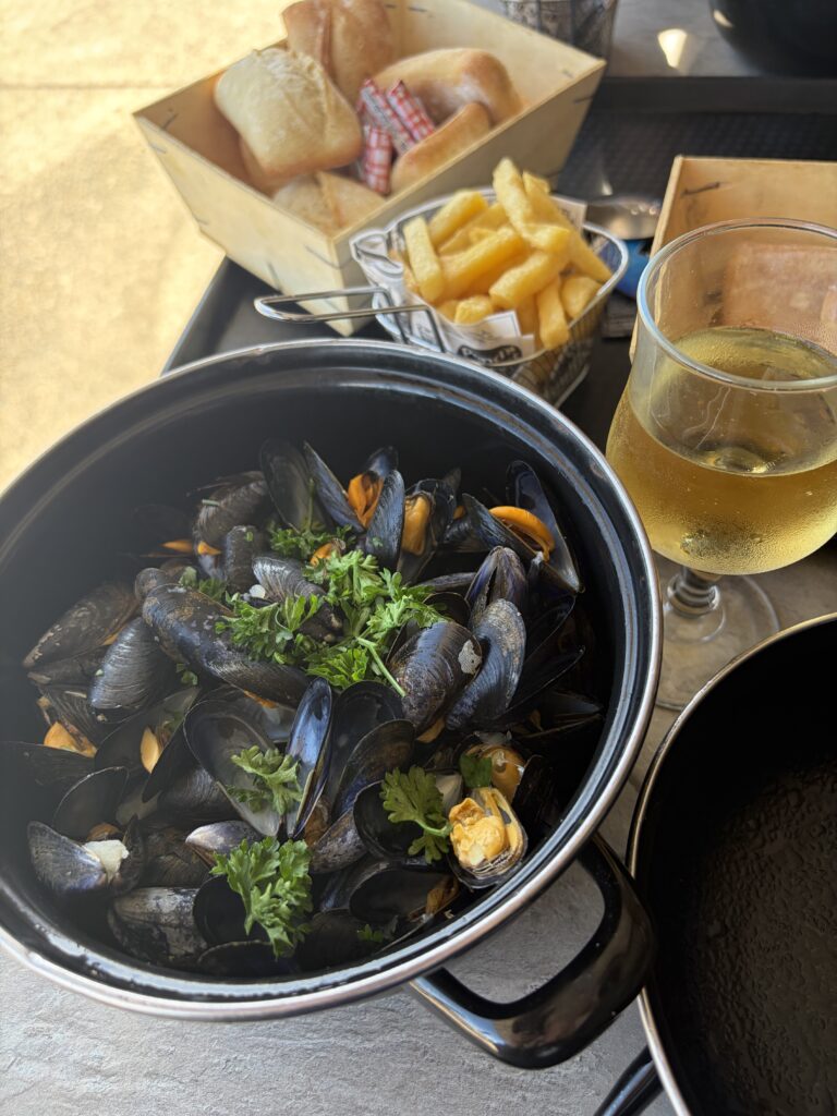 Frische Miesmuscheln mit Petersilie im schwarzen Topf, serviert mit Pommes frites, Baguette und einem Glas Weißwein in Hirel in der Bretagne.