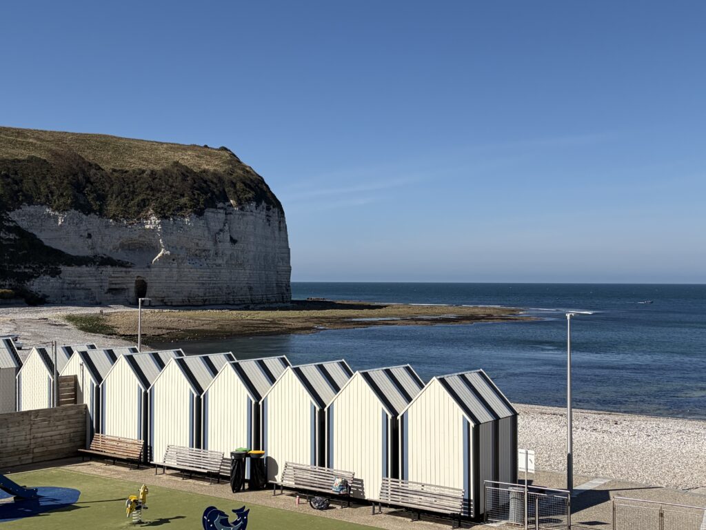 Strand von Saint-Valery-en-Caux in der Normandie mit weißen Strandkabinen, Kreidefelsen und Blick auf den Ärmelkanal.