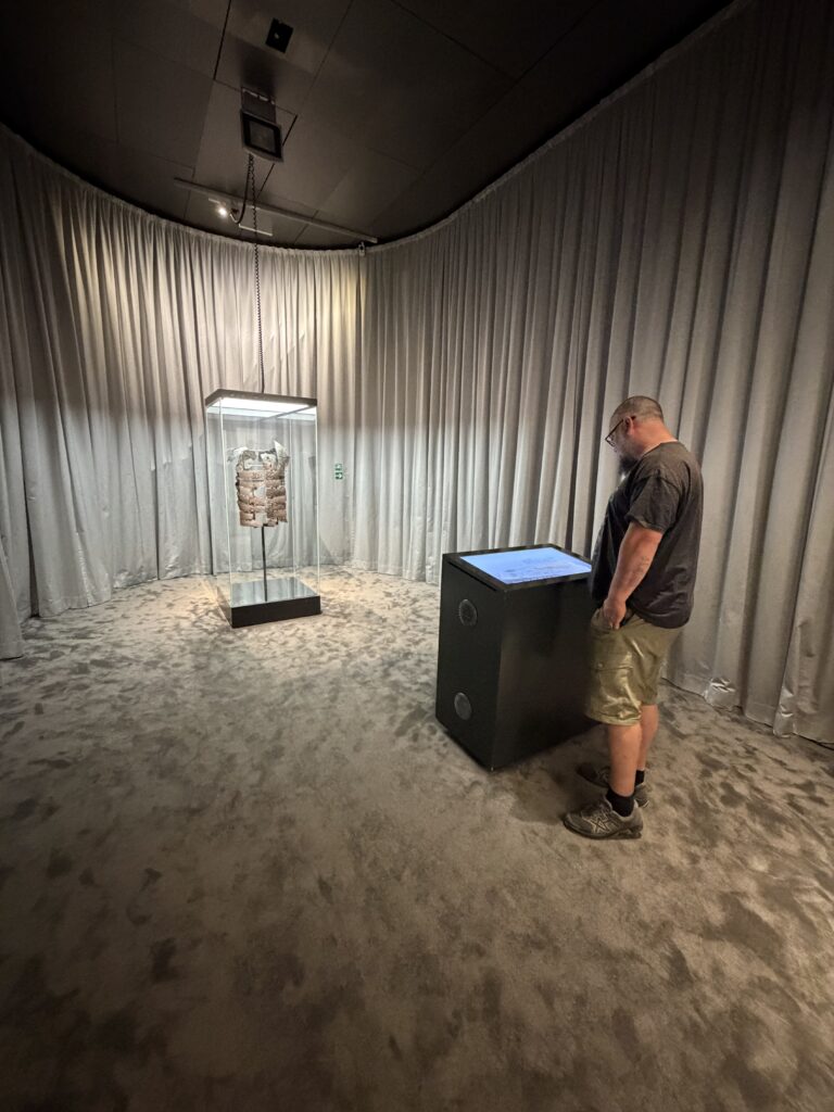 Besucher an einer interaktiven Informationsstation im Varusschlacht-Museum Kalkriese bei Bramsche, neben einer Glasvitrine mit archäologischem Fundstück aus römischer Zeit.