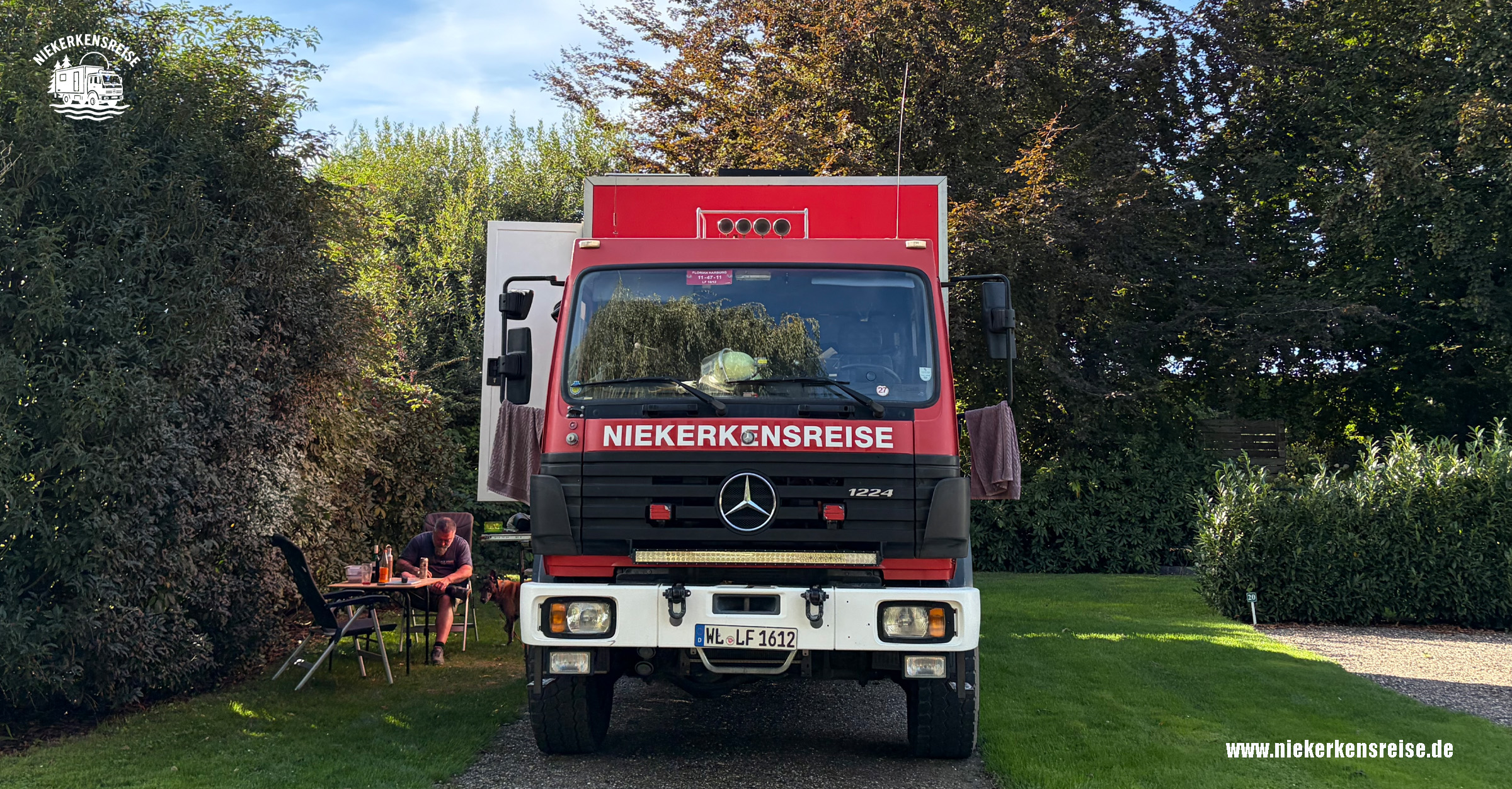 Roter Mercedes-Benz 1224 Expeditions-Lkw von Niekerkensreise auf einem begrünten Wohnmobilstellplatz in Kessel, Limburg, Niederlande.
