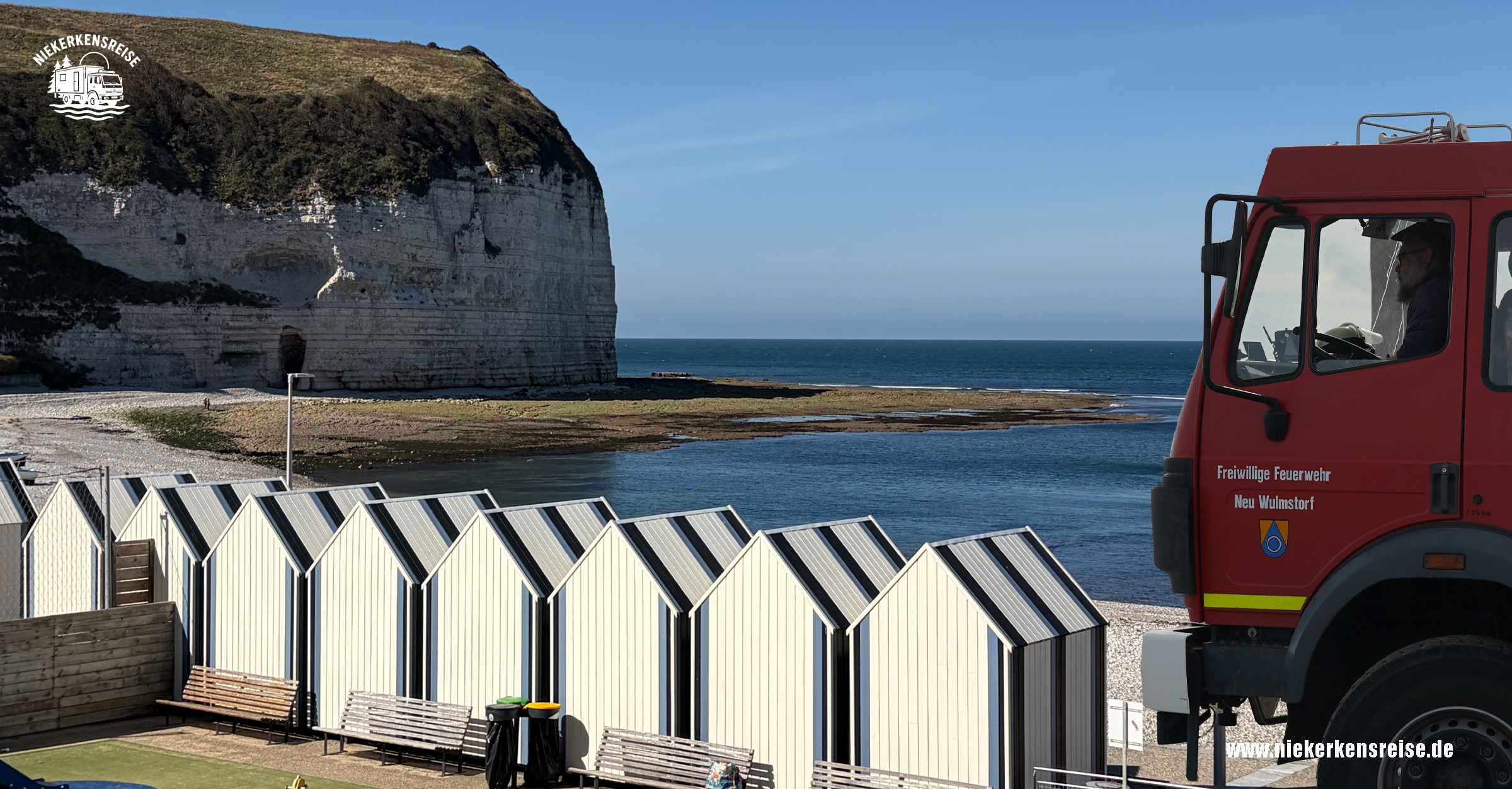 Mit dem Expeditionsmobil in Yport – Camping an der Alabasterküste Roter Mercedes-Benz Expeditions-LKW von Niekerkensreise vor den weißen Strandkabinen von Yport in der Normandie. Im Hintergrund die imposanten Kreidefelsen der Alabasterküste und das Meer.