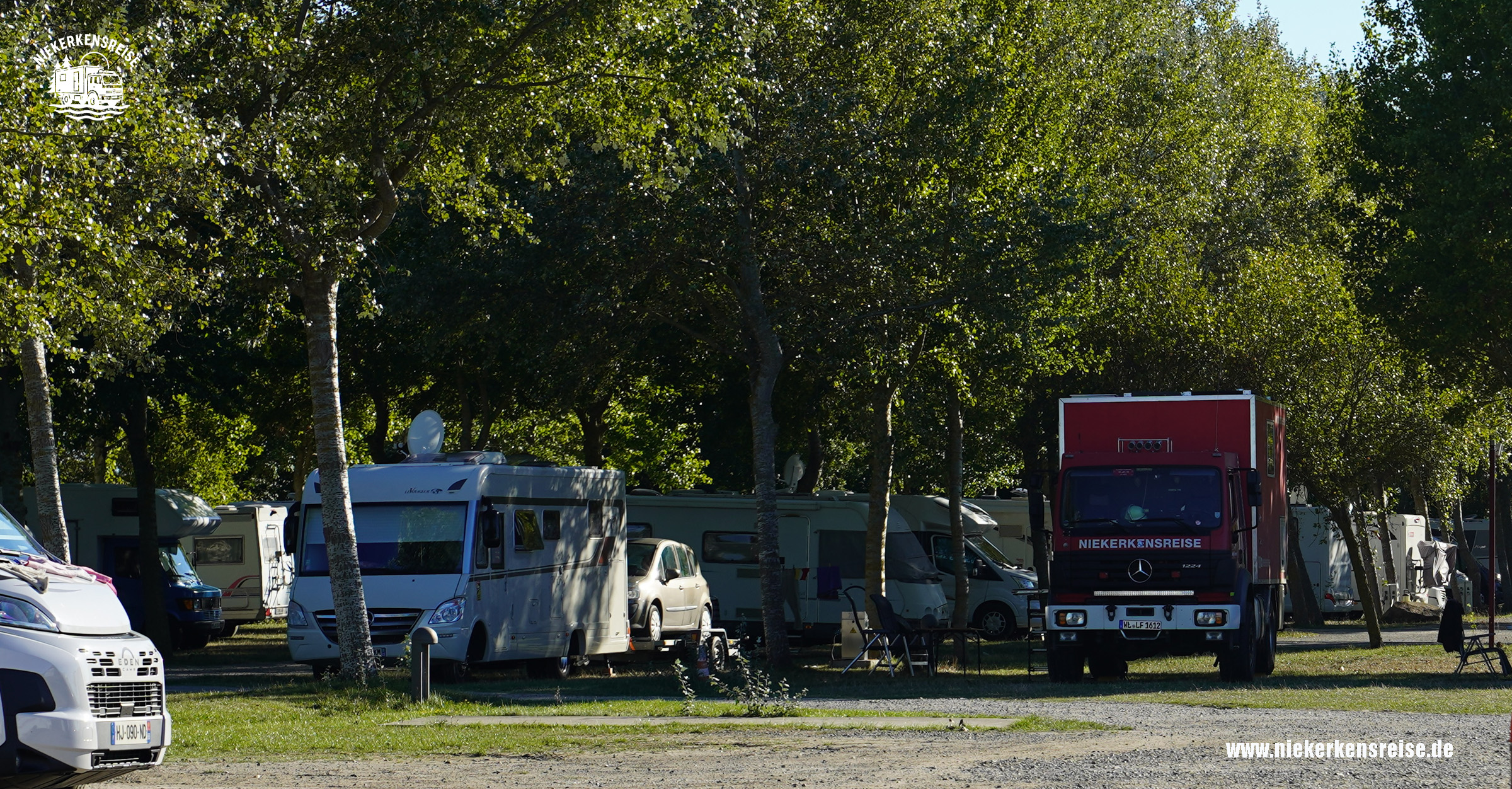 Camping-Car Park Hirel – Wohnmobilstellplatz La Ville és Brune in der Bretagne Wohnmobilstellplatz Camping-Car Park La Ville és Brune in Hirel, Bretagne, mit schattigen Stellplätzen unter Bäumen und dem roten Expeditionsmobil von Niekerkensreise.