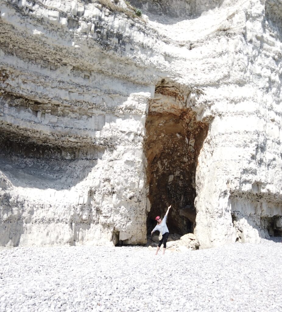 Gewaltige weiße Kreidefelsen am Kieselstrand von Yport in der Normandie. Eine Person steht vor einer großen Felsspalte in der Steilküste der französischen Alabasterküste.
